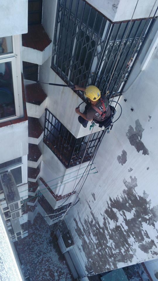 Persona con equipo de seguridad descendiendo en rapel por el exterior de un edificio, con casco amarillo y arnés negro.