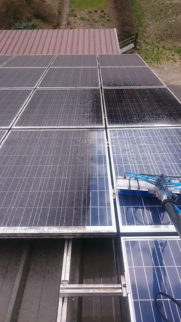 Auf einem Dach werden Solarpaneele gereinigt. Ein Teil ist nass und sauber, ein anderer verschmutzt.