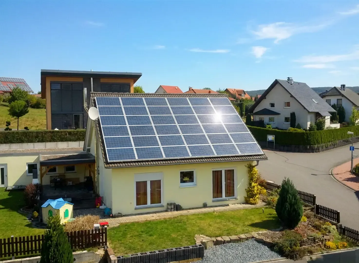 Gelbes Haus mit Solarpaneelen auf dem Dach, grüner Rasen, blauer Himmel und andere Häuser im Hintergrund.