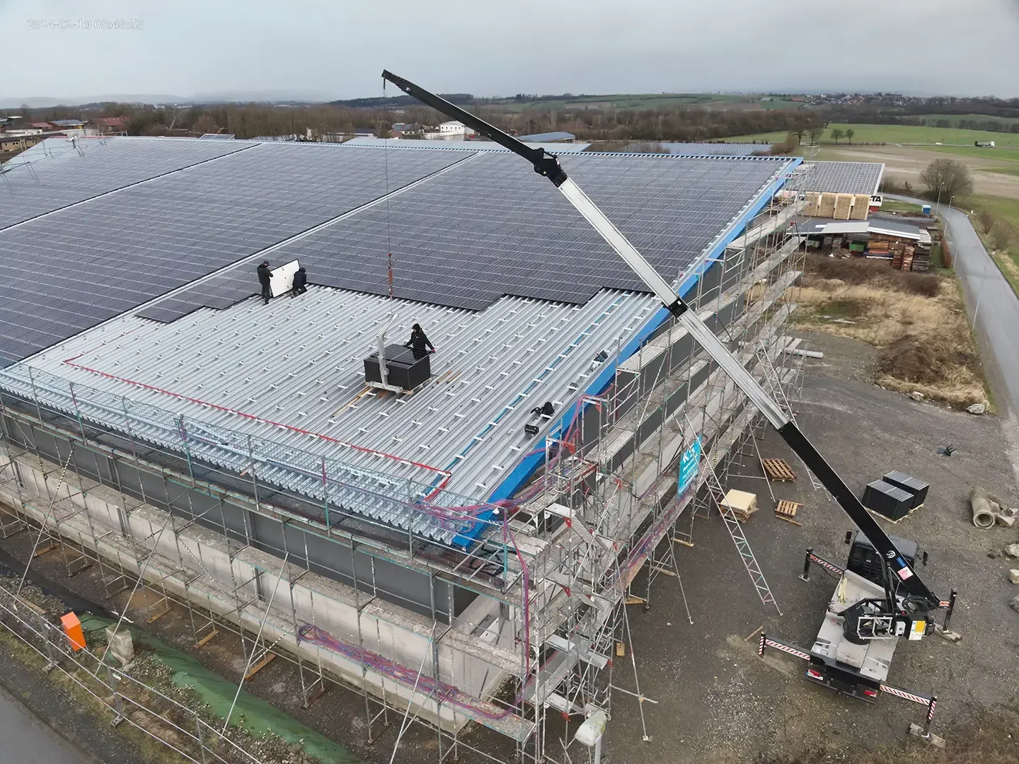 Bau eines Gebäudes mit Solarpaneelen auf dem Dach, Kran hebt Baumaterialien an.