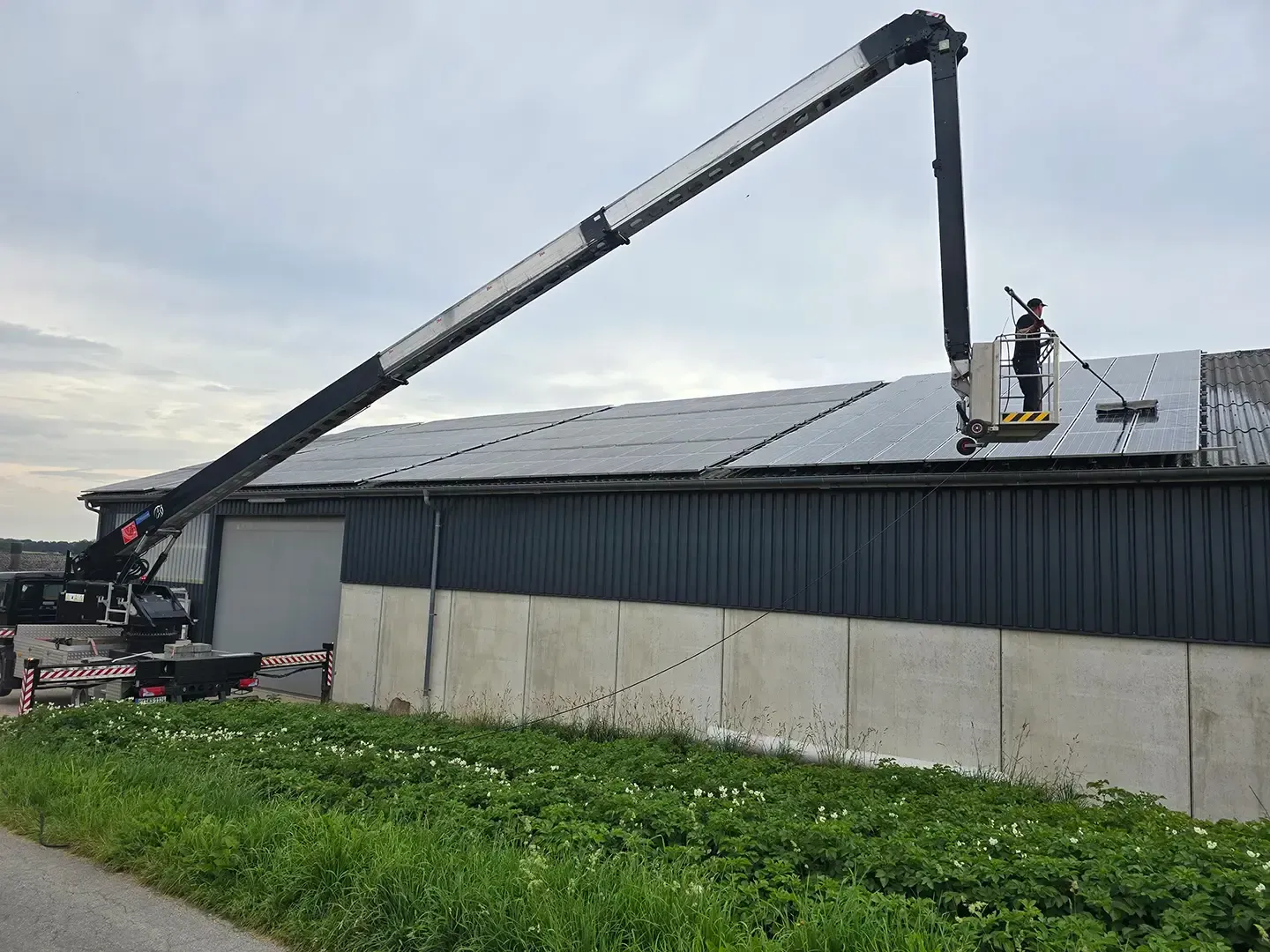 Eine Person arbeitet in einem Aufzug an Solarmodulen auf dem Dach eines Gebäudes. Der Kran ist ausgefahren. Bewölkter Tag.