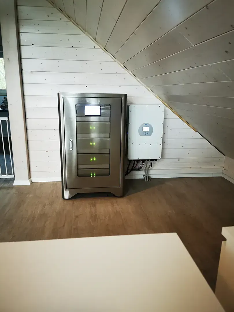 Silberne Batteriespeichereinheit und weißer Wechselrichter auf einem mit Holz verkleideten Dachboden.