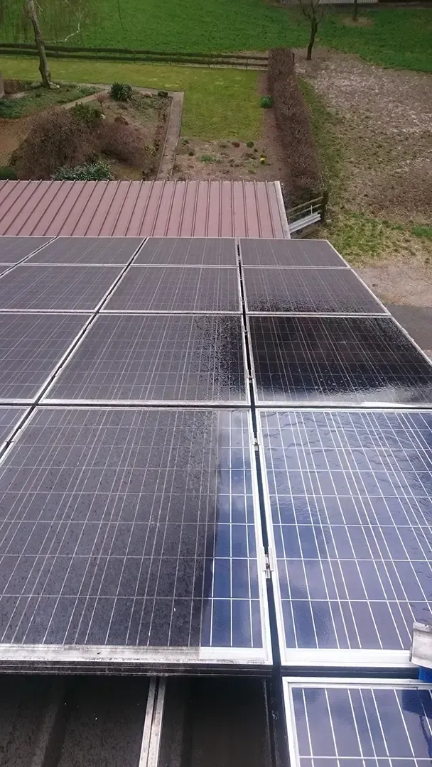 Solarpaneele auf einem teilweise gereinigten Dach spiegeln den Himmel wider. Braunes Dach und grüner Garten im Hintergrund.