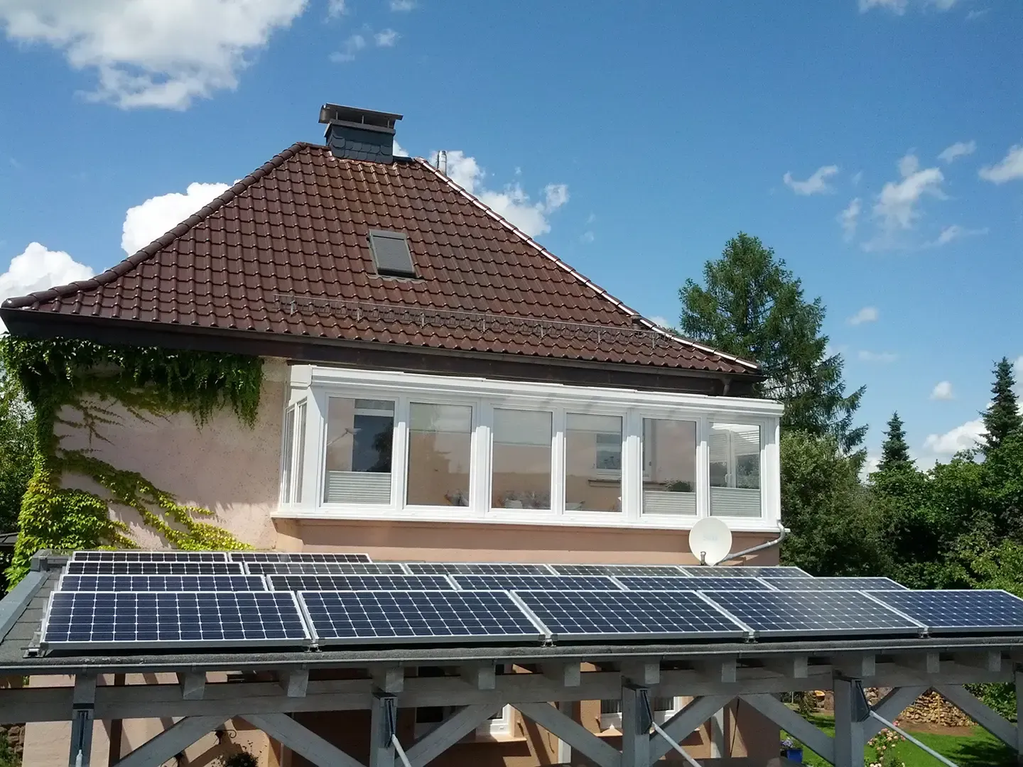 Solarpaneele auf einer Holzkonstruktion unterhalb eines Hauses mit einem weißen Wintergarten.