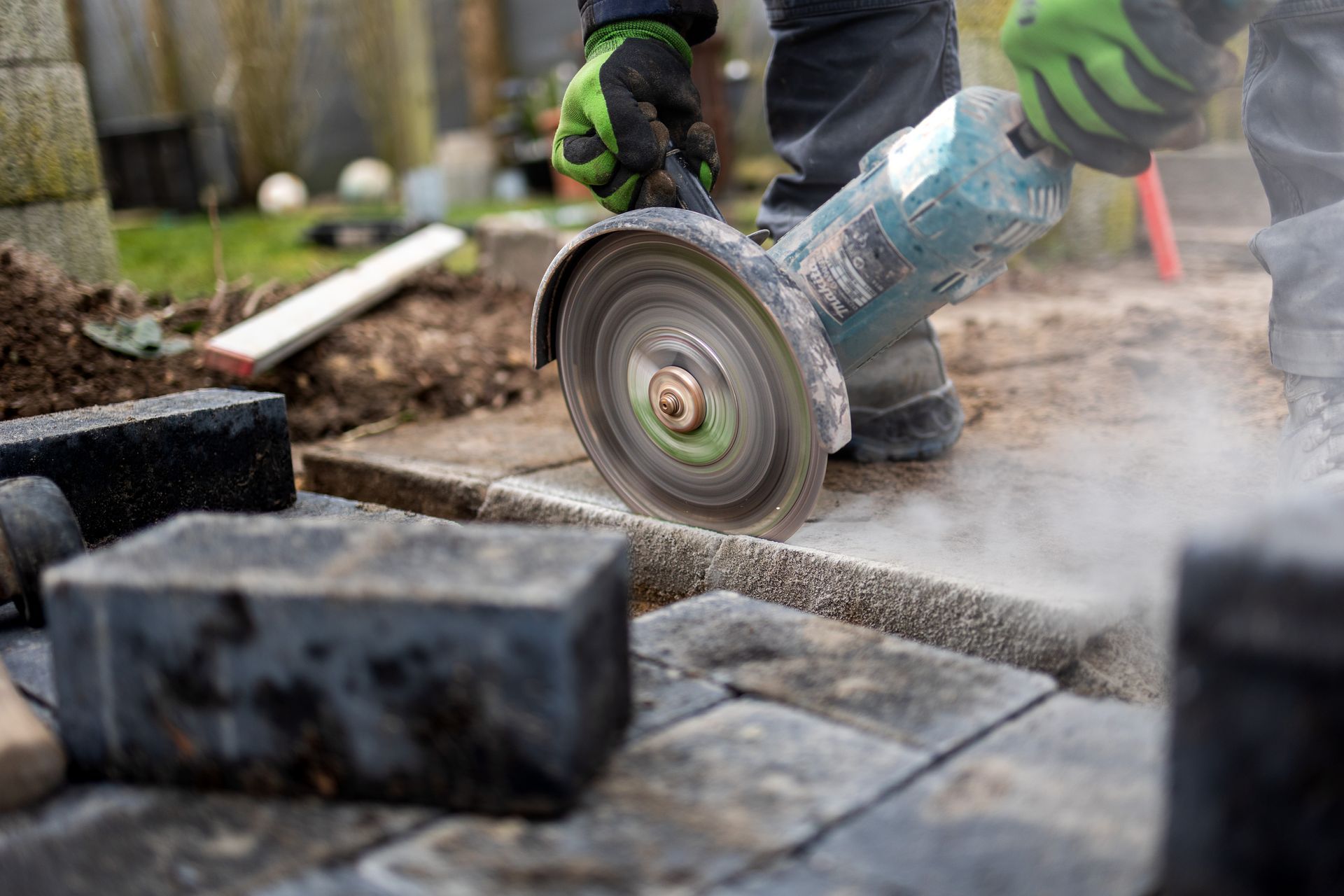 Eine Person schneidet mit einer Schleifmaschine Ziegelsteine auf einem Gehweg.