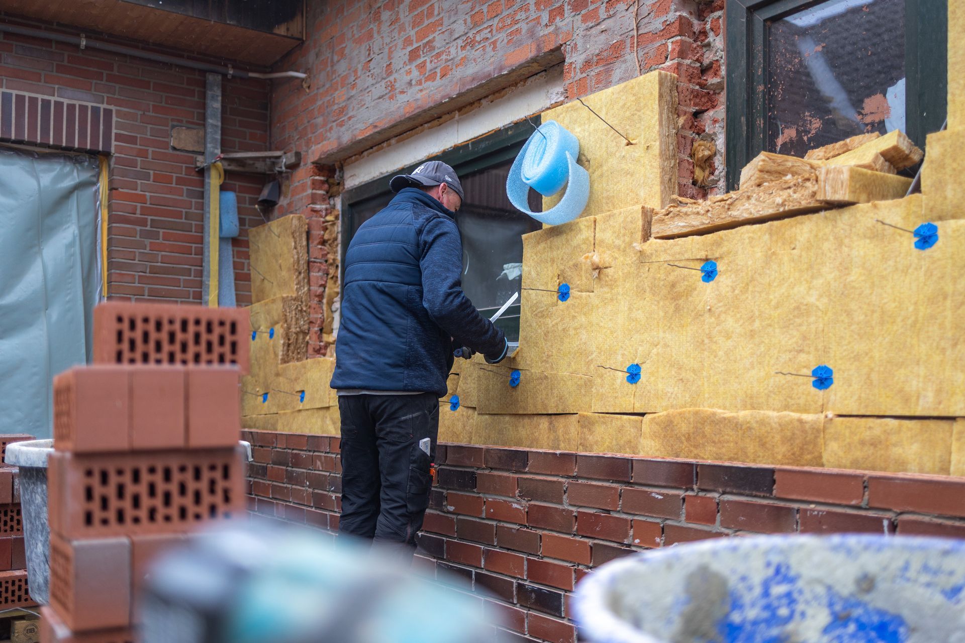 Ein Mann bringt eine Isolierung an einer Ziegelwand an.