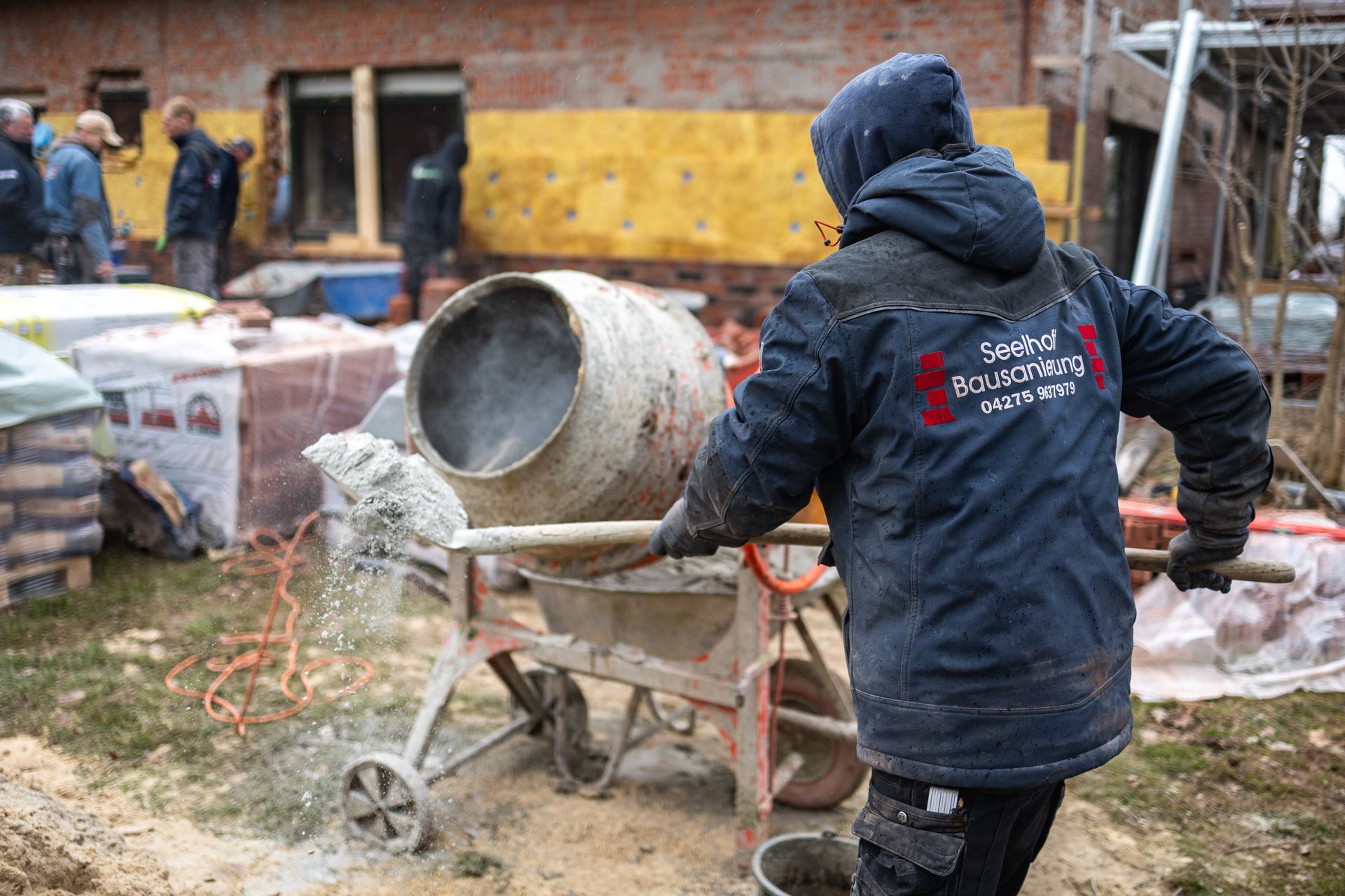 Ein Mann in einer blauen Jacke mischt Zement in einer Schubkarre.