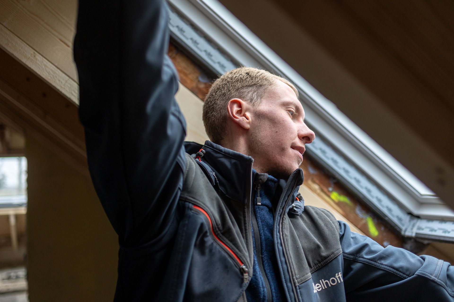 Ein Mann in einer Jacke steht vor einem Fenster.