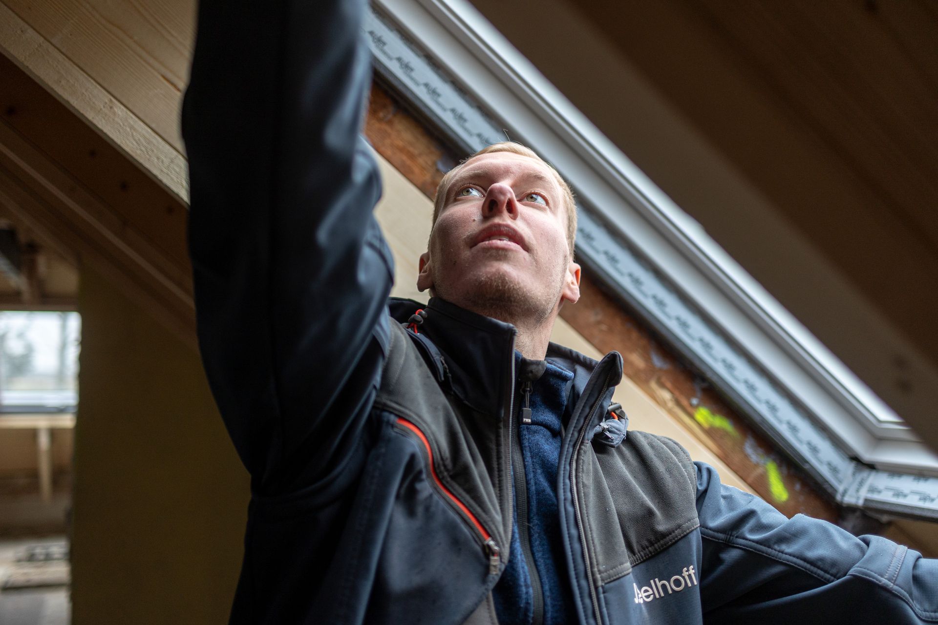 Ein Mann in einer blauen Jacke steht vor einem Fenster.