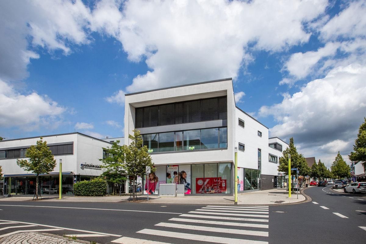 An einer Straßenecke steht ein weißes Gebäude mit vielen Fenstern.