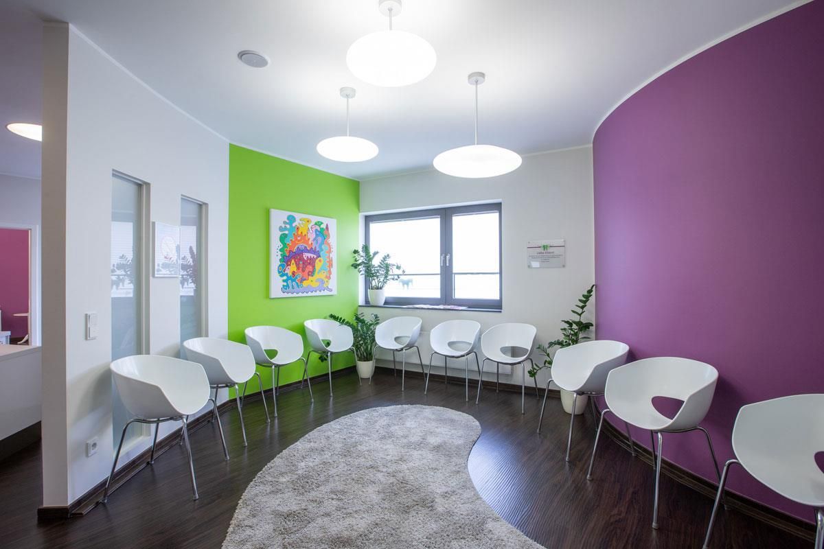 Ein Wartezimmer mit violetten und grünen Wänden und weißen Stühlen