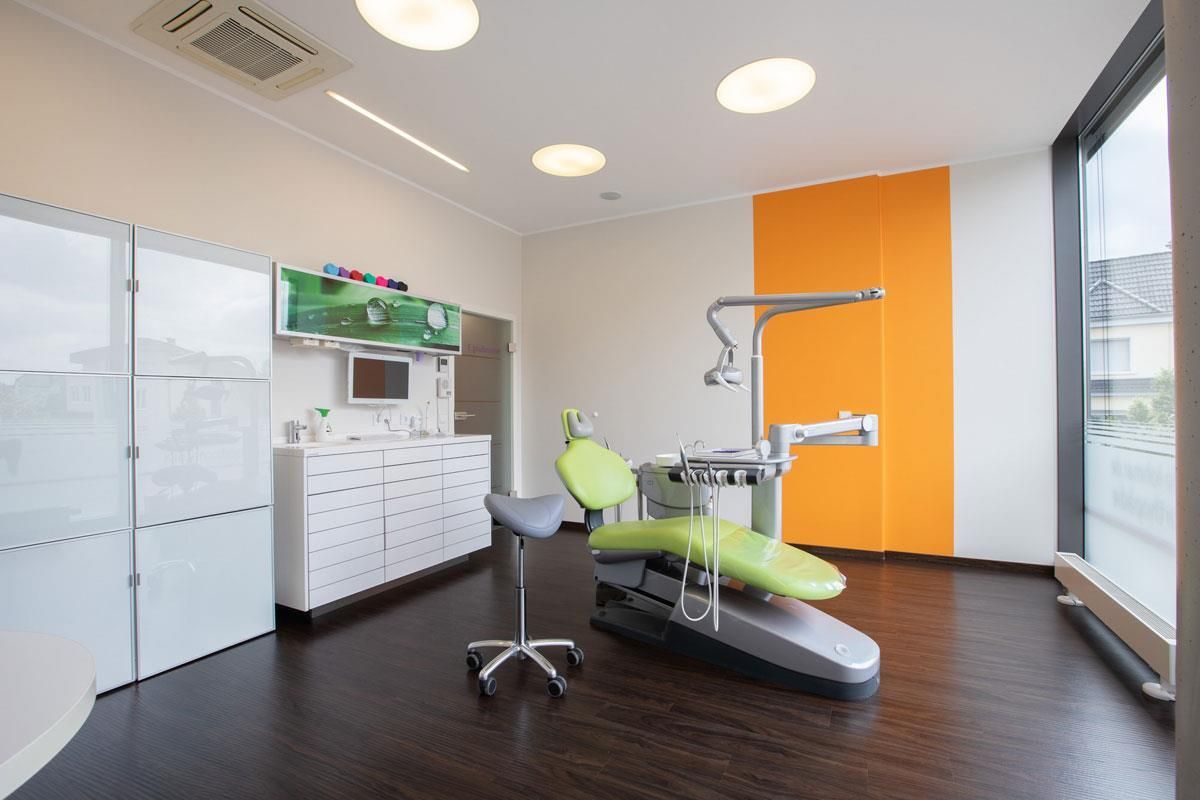 Eine Zahnarztpraxis mit einem grünen Zahnarztstuhl und einem großen Fenster.