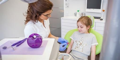 Ein kleines Mädchen sitzt auf einem Zahnarztstuhl und lässt seine Zähne von einem Zahnarzt untersuchen.