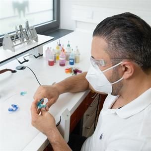 Ein Mann mit Maske und Brille sitzt an einem Schreibtisch.