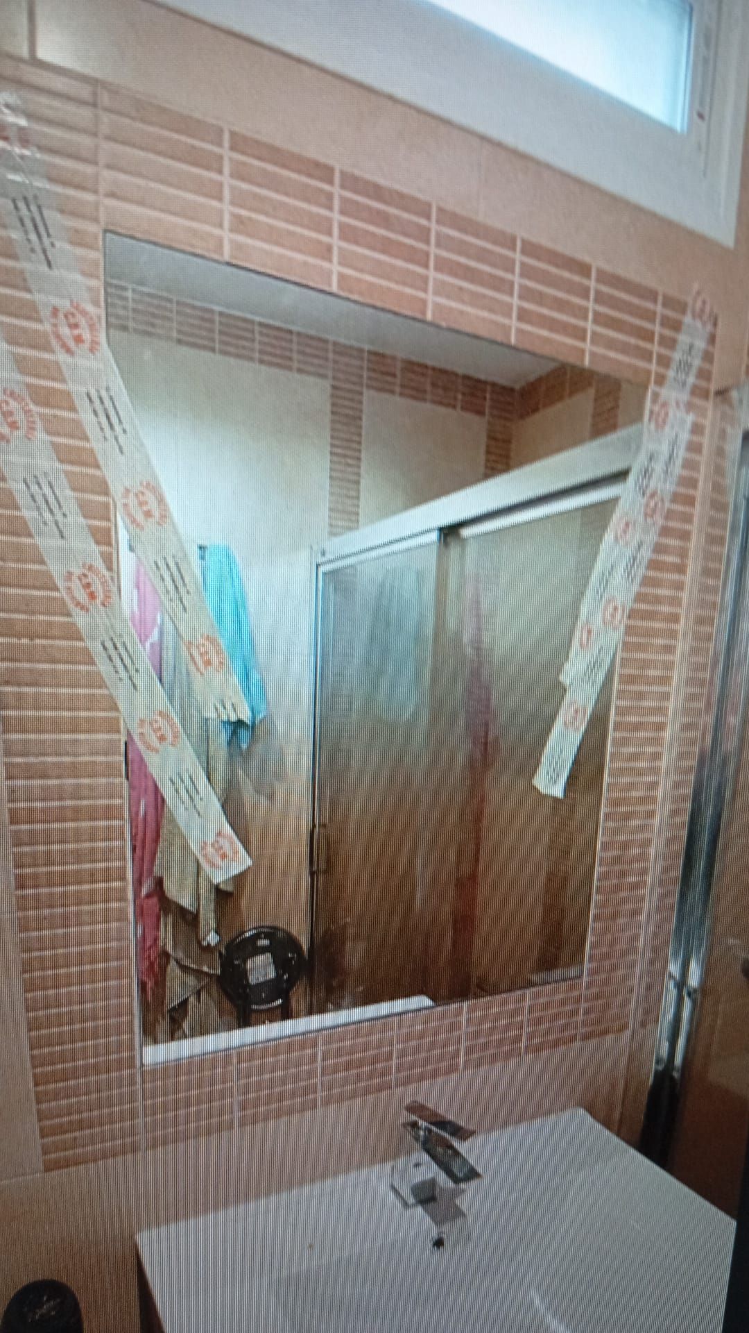 Baño con paredes alicatadas, gran espejo, ducha y lavabo.