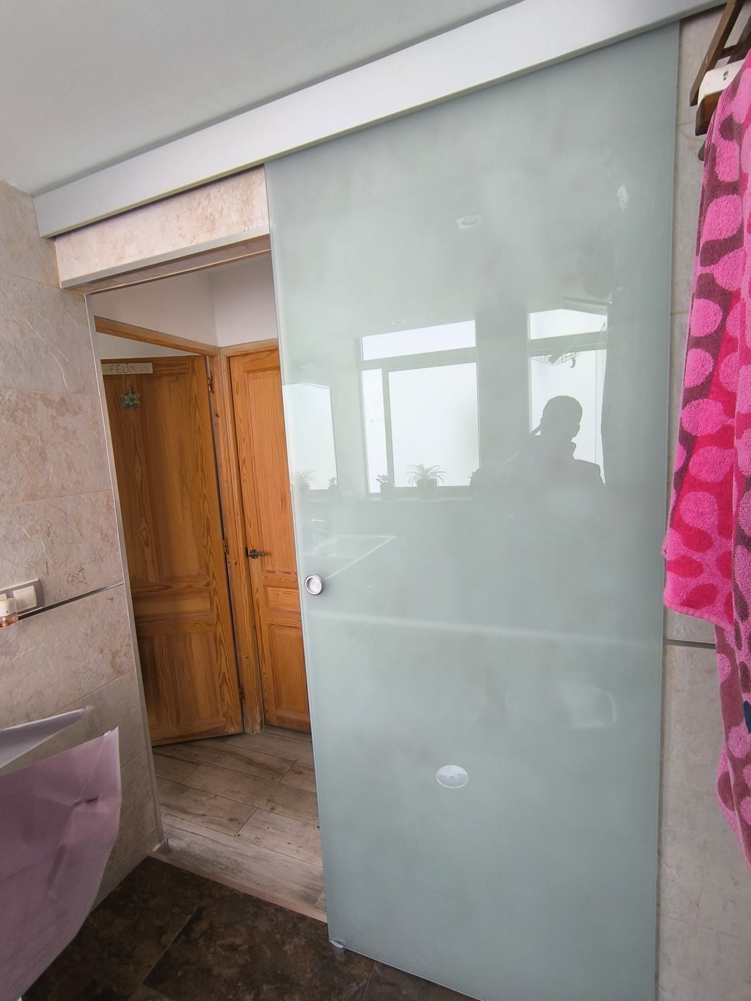 Puerta corrediza de vidrio esmerilado en el interior. Revela un pasillo con puertas de madera. Una tela rosa cuelga a la derecha.