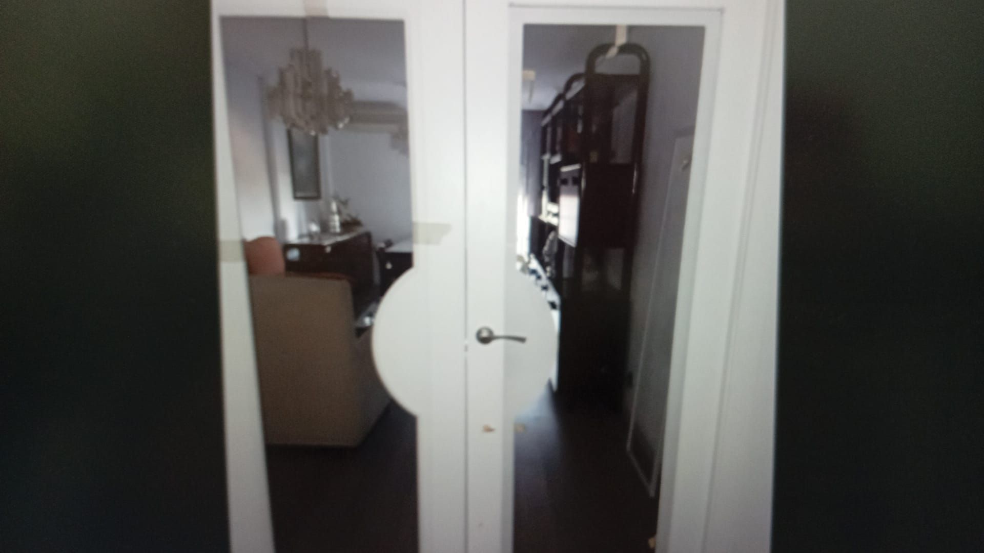 Puertas dobles de vidrio blanco que reflejan una lámpara de araña, una sala de estar y una estantería de madera oscura.