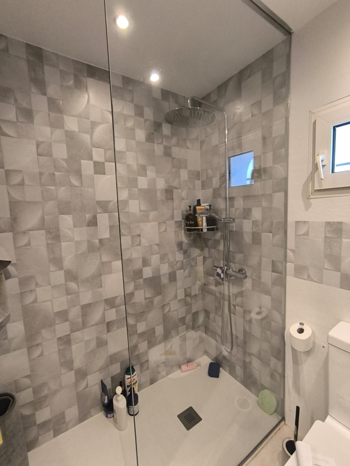 Una ducha de baño moderna con paredes de azulejos grises, puerta de vidrio y artículos de tocador.
