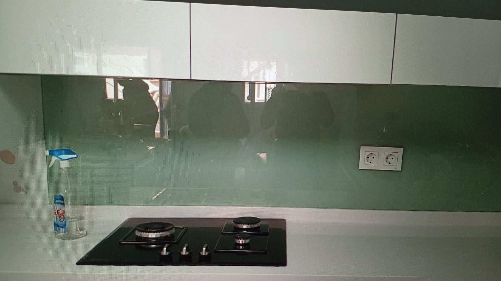 Salpicadero de cocina con panel de vidrio verde y gabinetes blancos sobre una estufa.