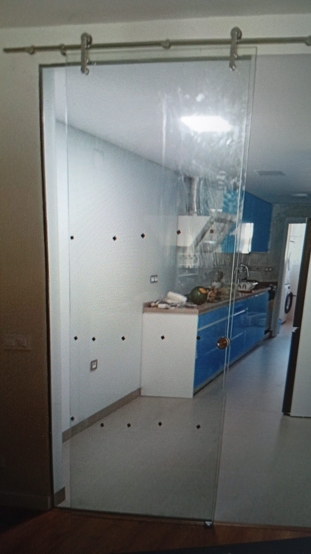 Puerta corrediza de vidrio, herrajes de acero inoxidable, que separa la cocina con gabinetes azules de una habitación.