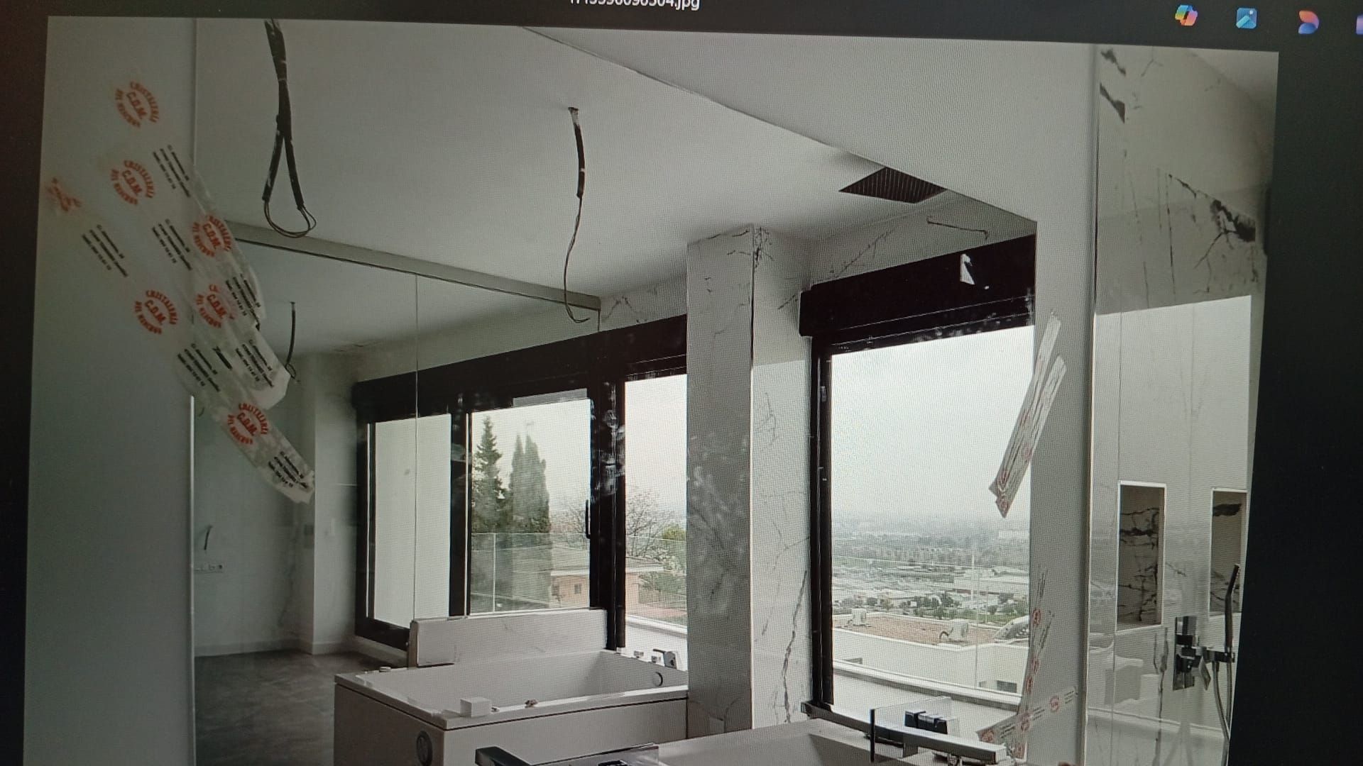 Interior de una habitación con grandes ventanales, paredes y techo sin terminar. Cielo nublado visible en el exterior.