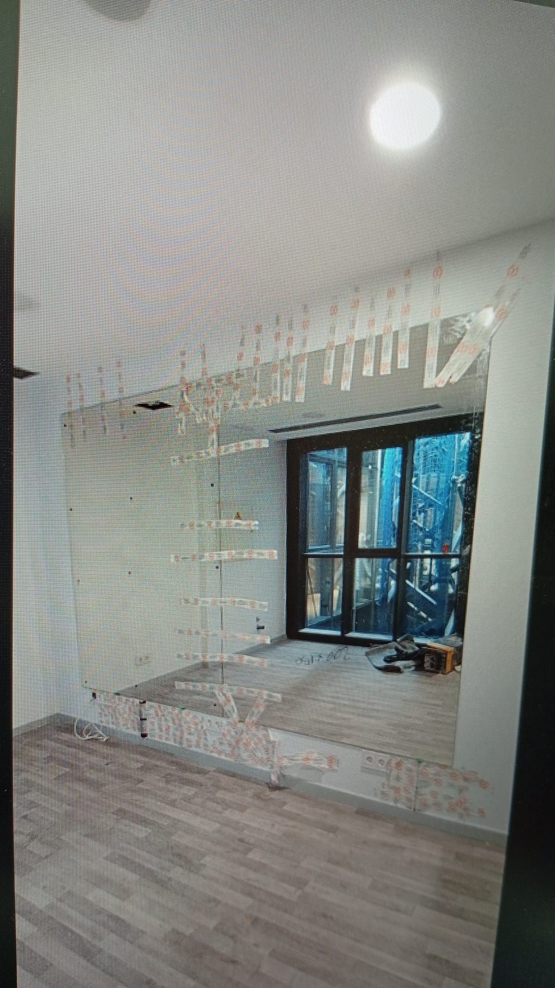 Interior de una habitación en construcción con un gran ventanal con vista a un bosque; piso de madera clara, paredes blancas.