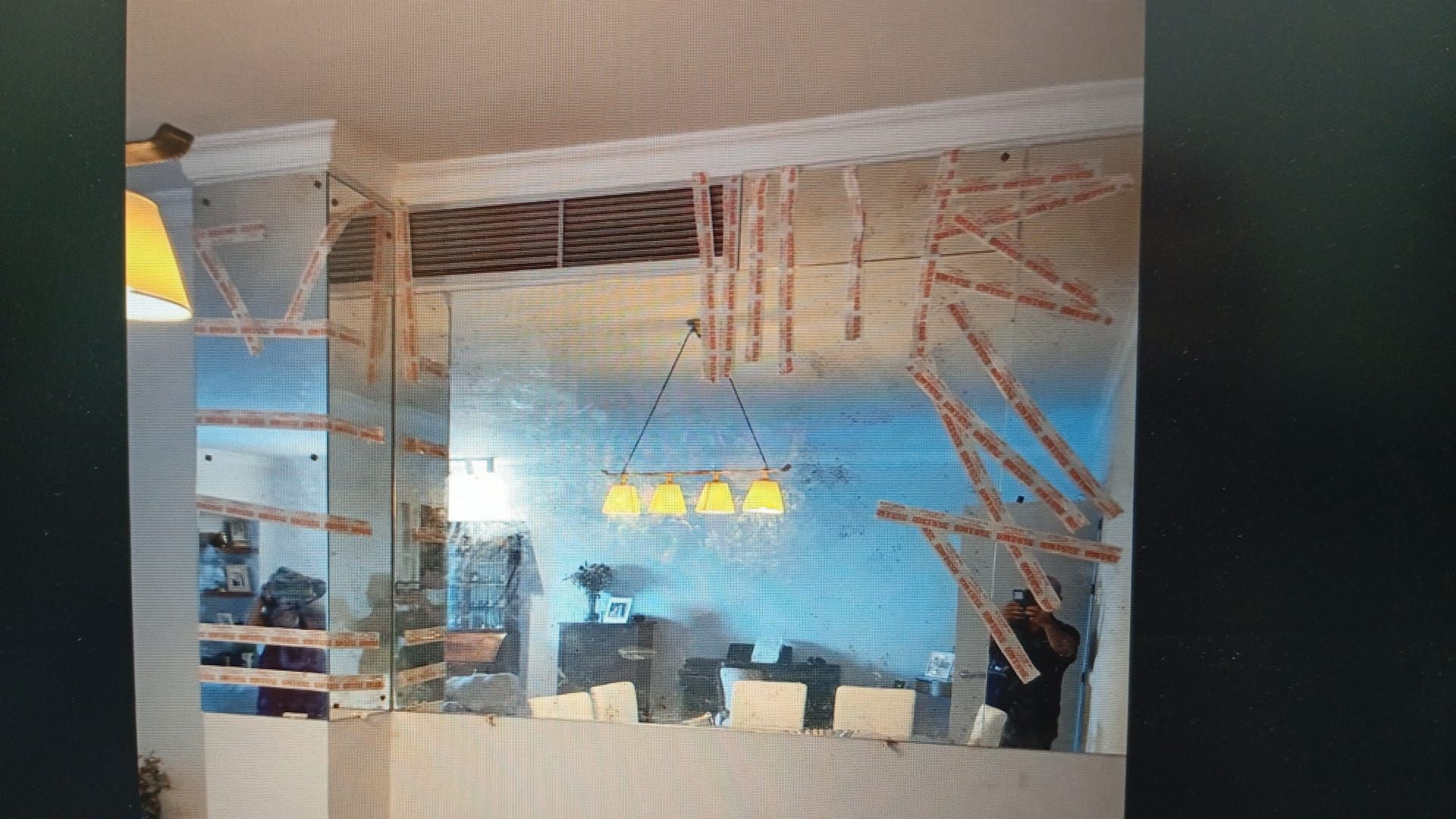 Una habitación con una gran pared de espejos, una mesa de comedor y vigas del techo rotas.