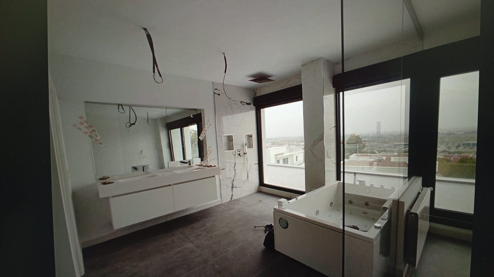 Baño moderno con gran espejo, bañera y vista a la ciudad.