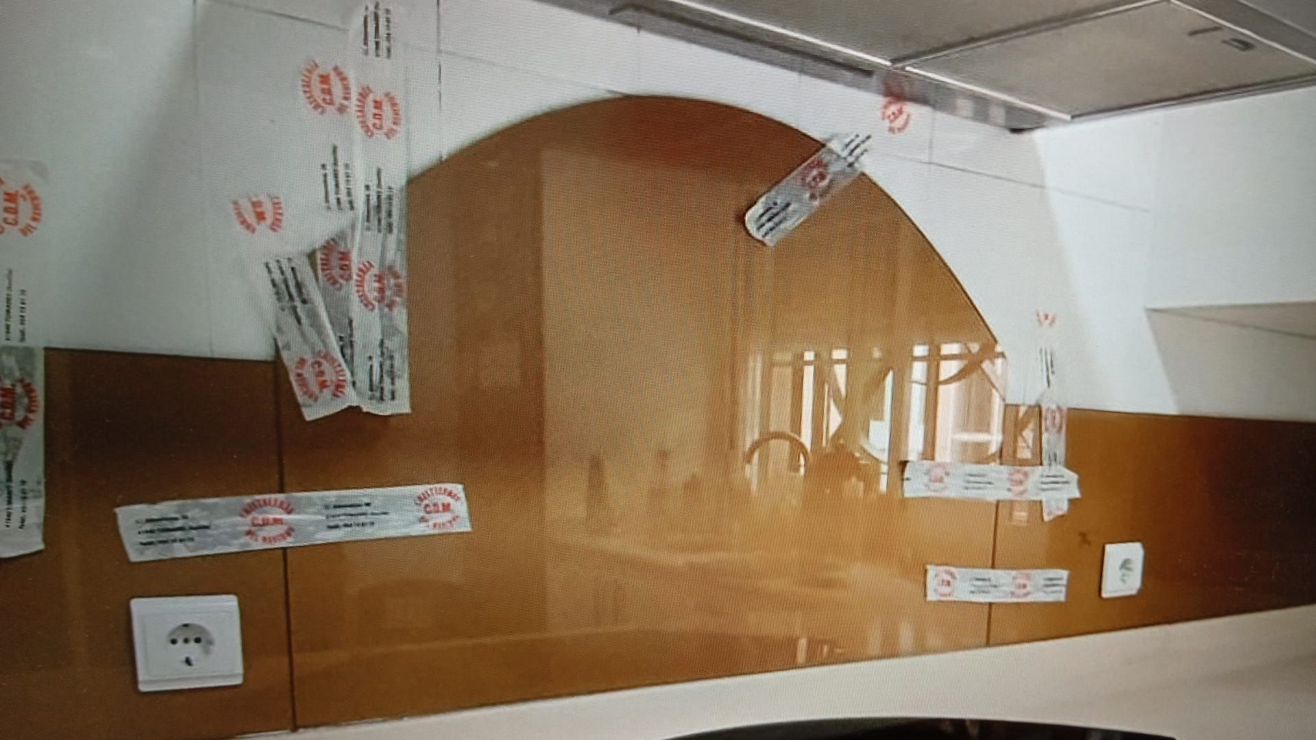 Un área de cocina con protector contra salpicaduras marrón, enchufes eléctricos y etiquetas de papel colgando del techo.