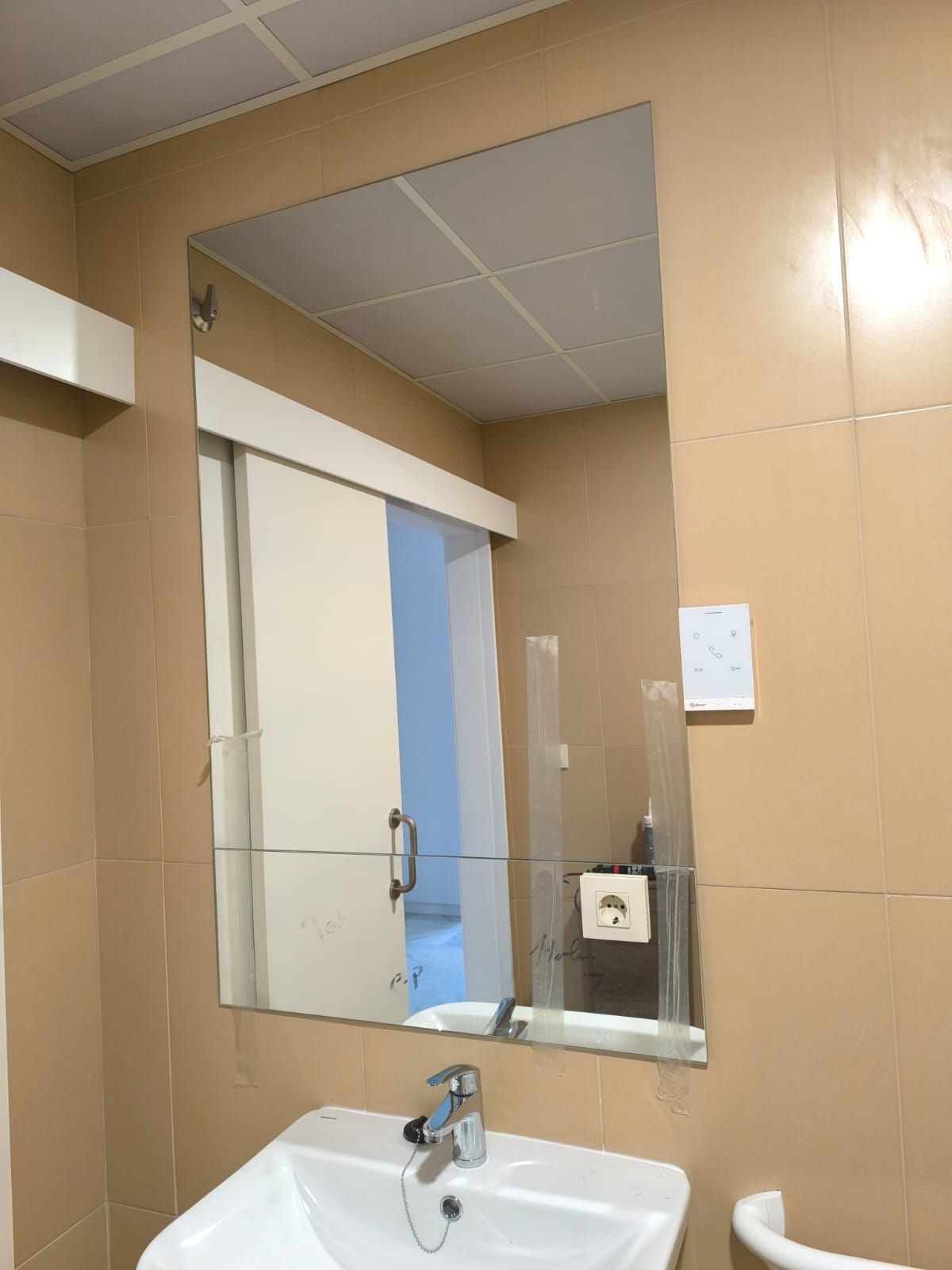 Espejo de baño sobre un lavabo, que refleja una puerta blanca y paredes de azulejos pálidos.