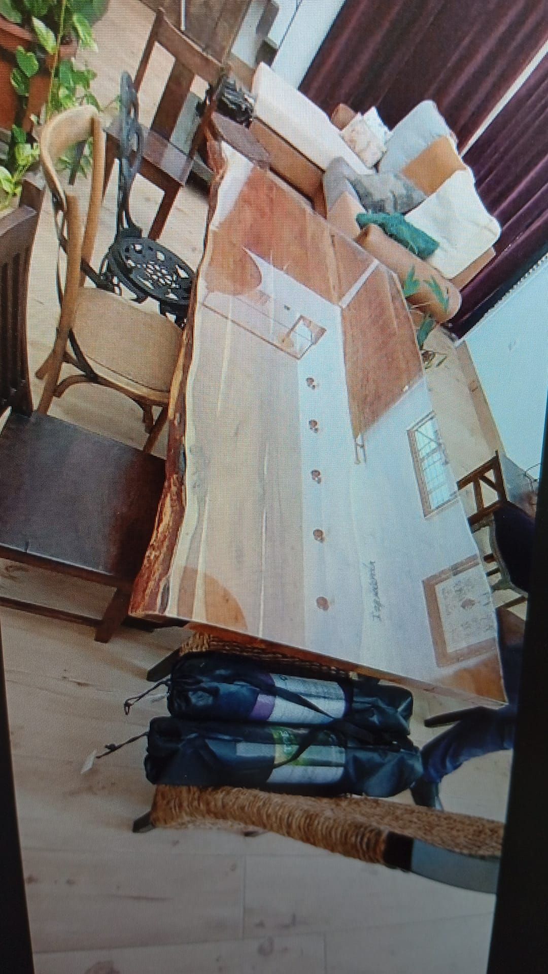 Mesa de exterior de madera con mantel estampado y dos bolsas de lona negras en el suelo.