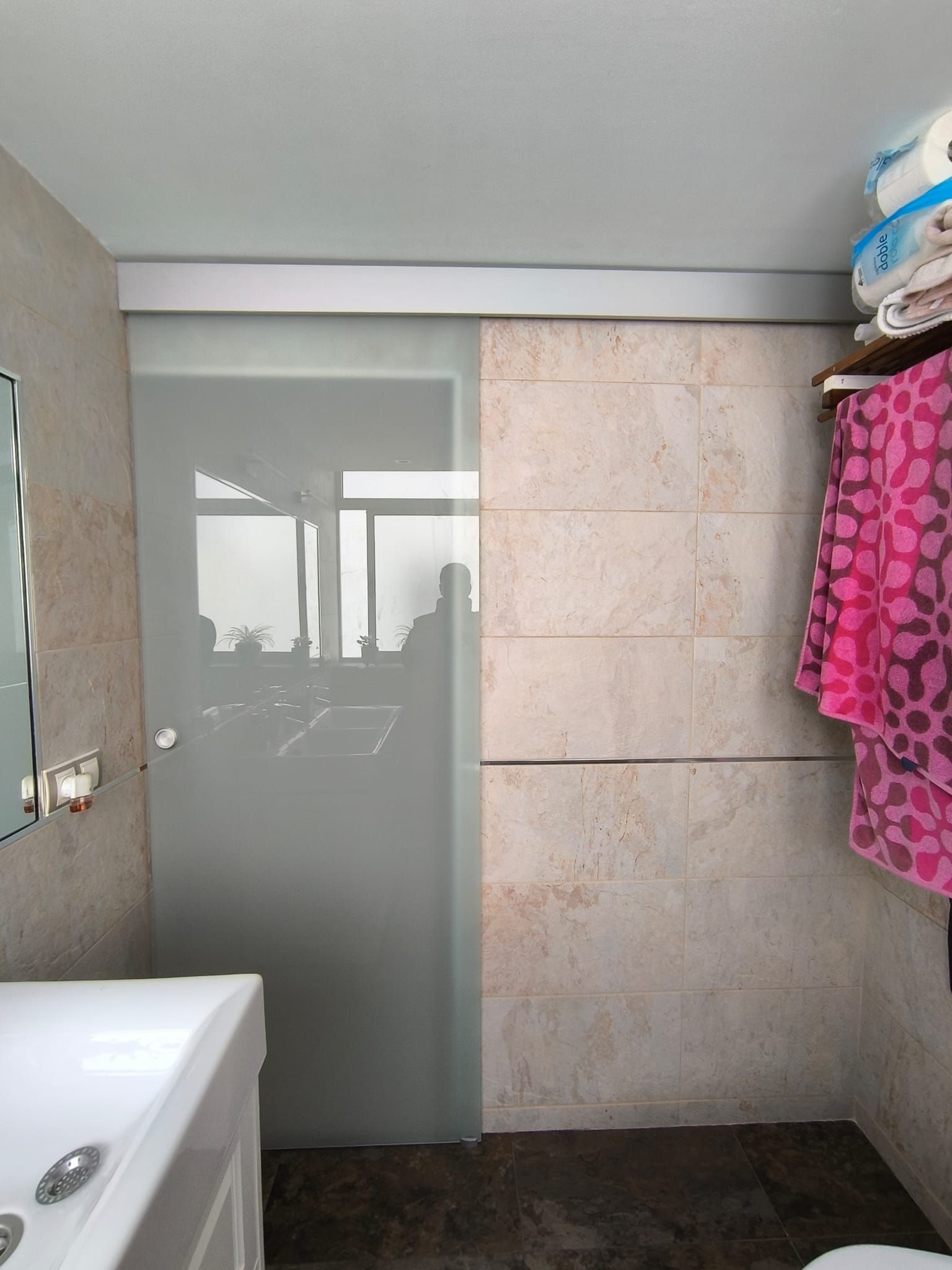 Baño con puerta corrediza de vidrio esmerilado, pared de piedra y lavabo. Toallas y sábanas en un estante.