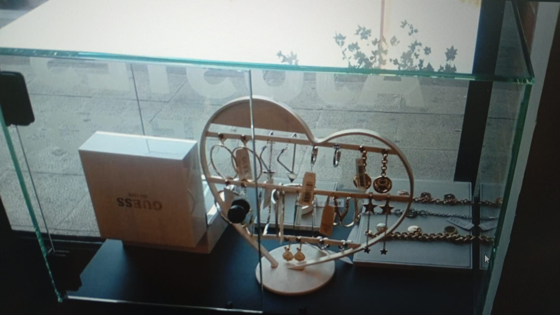 Vitrina de joyería con porta pendientes en forma de corazón, una caja blanca y algunas tiras de joyas.