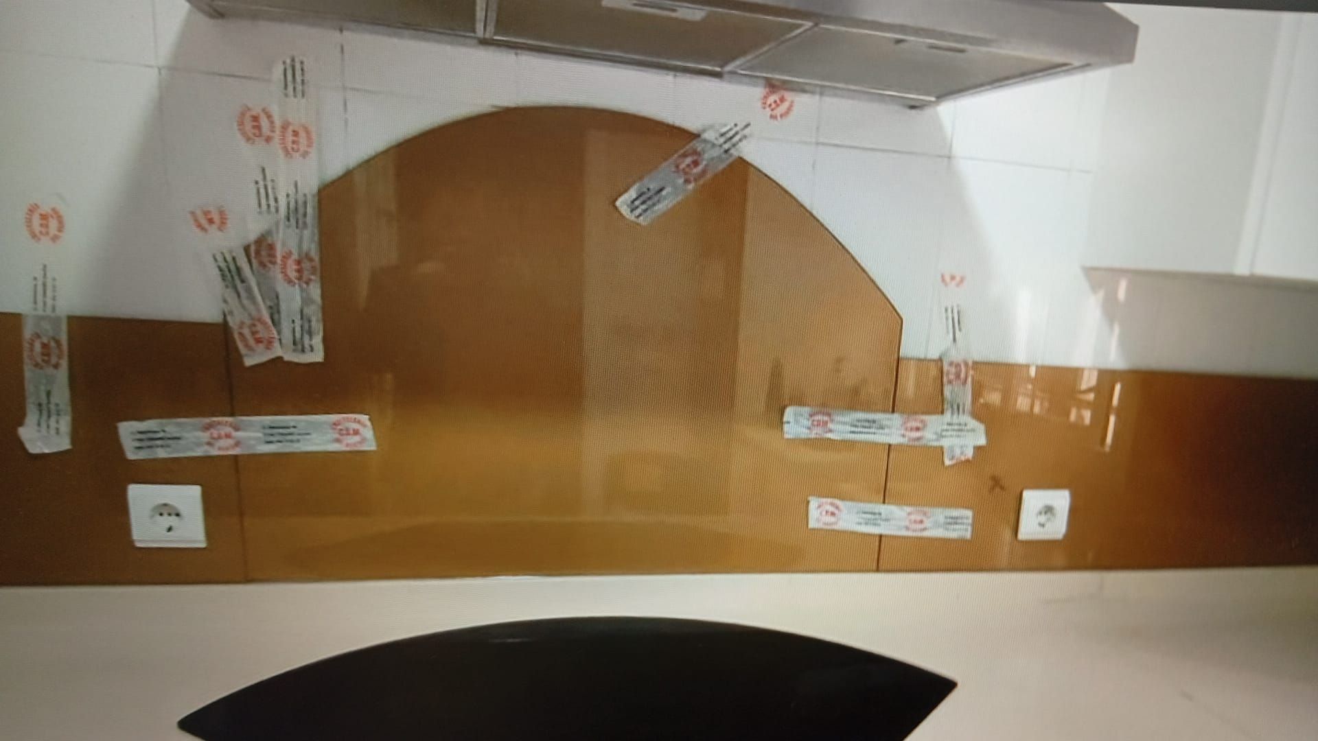 Salpicadero marrón con plantilla pegada con cinta debajo de una campana extractora y azulejos blancos.