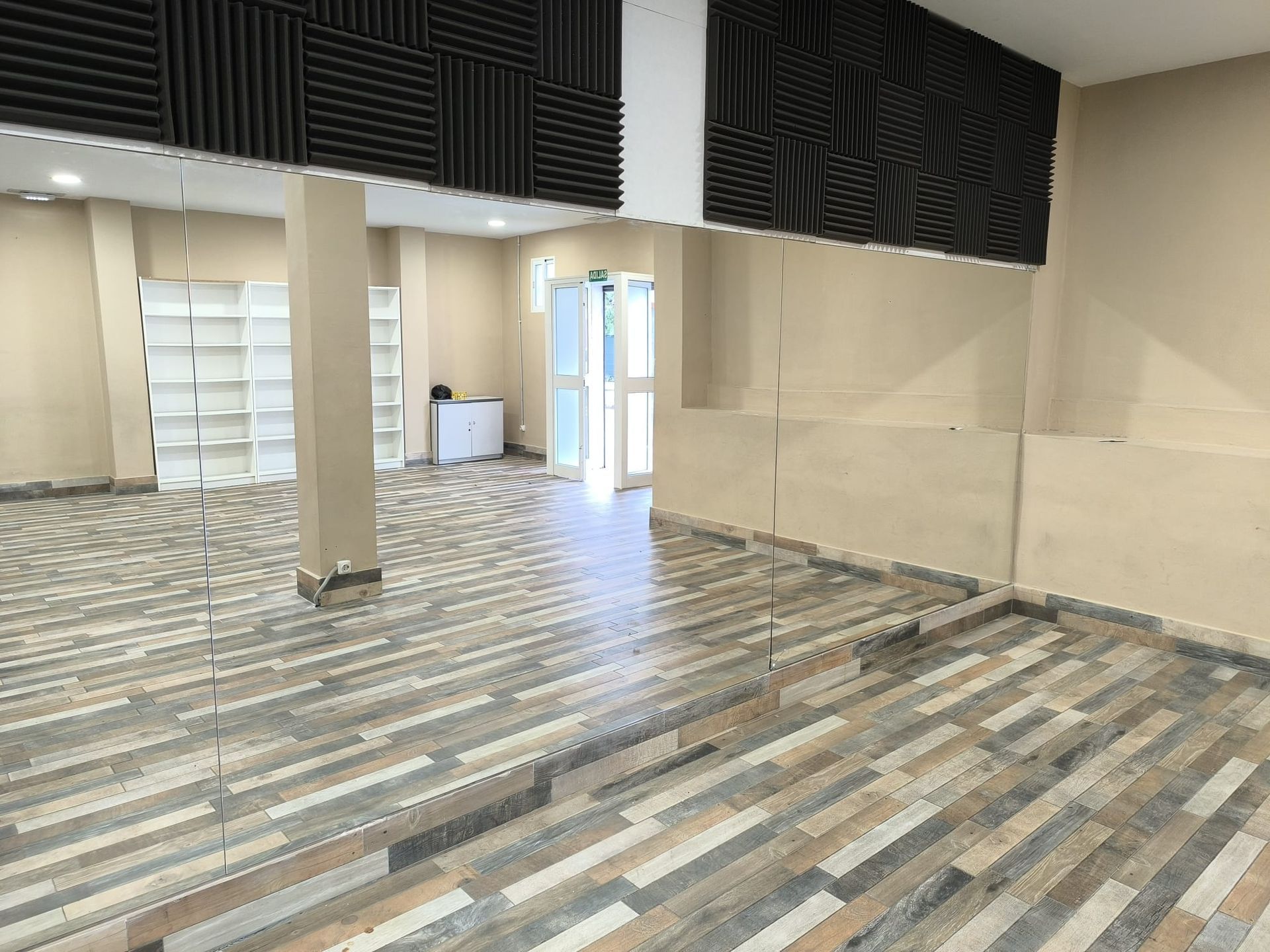 Habitación vacía con suelo imitación madera, paneles acústicos en la pared y estanterías.