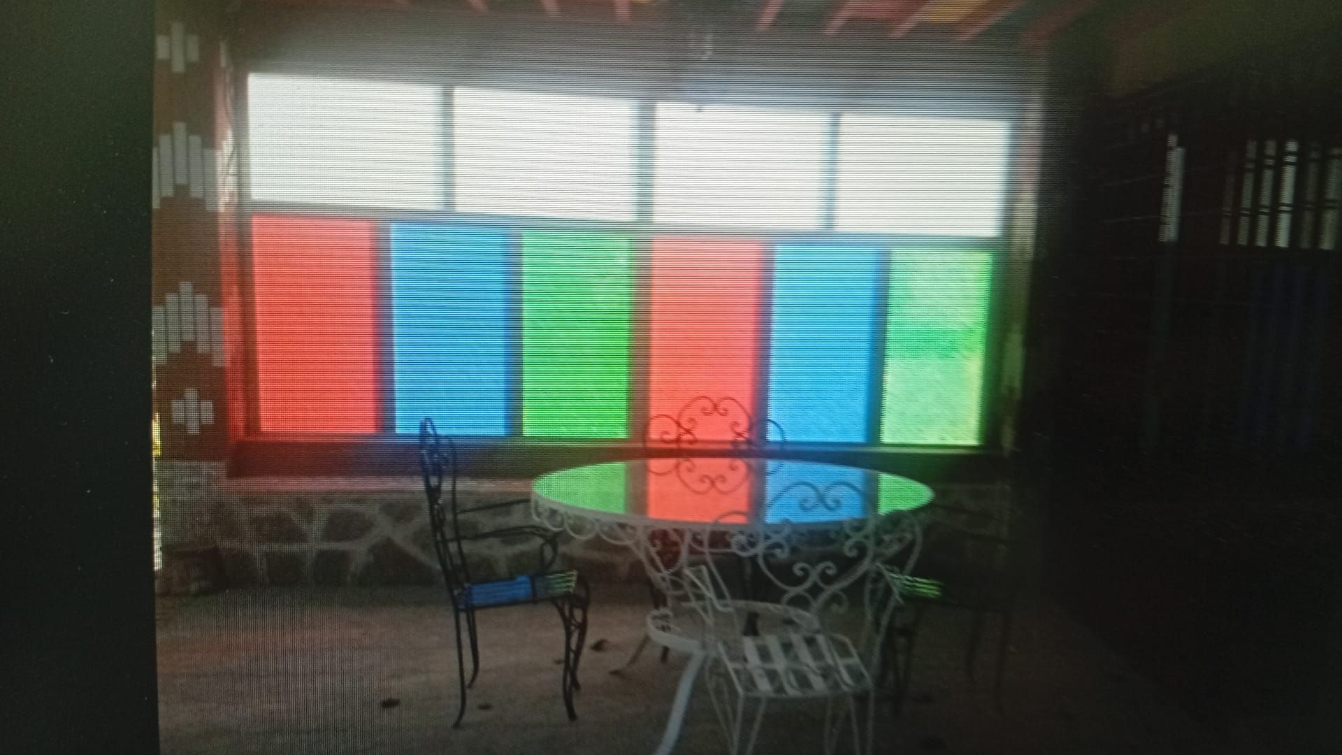 Una mesa y sillas se encuentran frente a una ventana colorida con paneles azules, verdes y rojos.