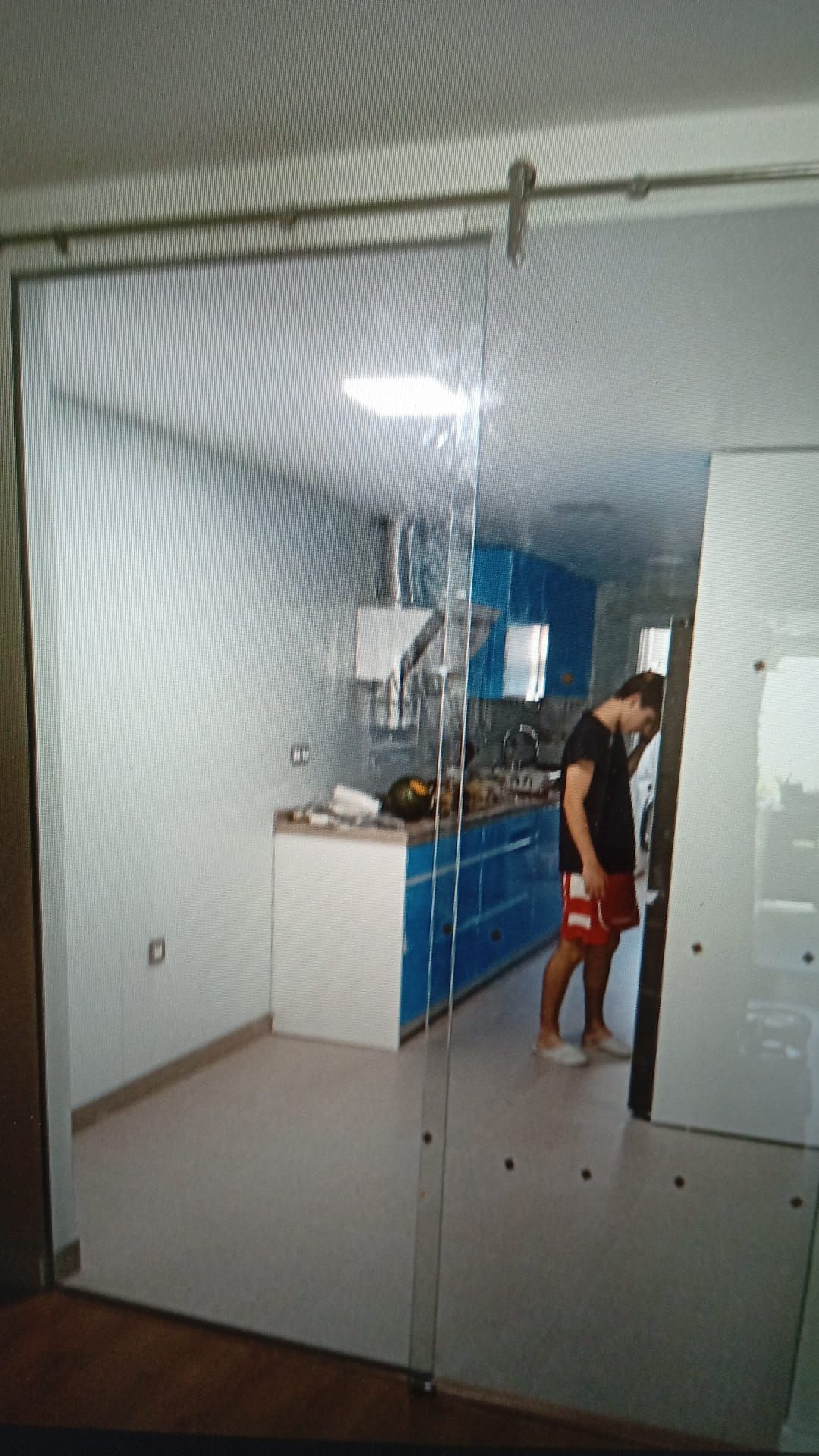 Puerta corrediza de vidrio que revela una cocina con gabinetes azules; una persona está parada cerca de la puerta.