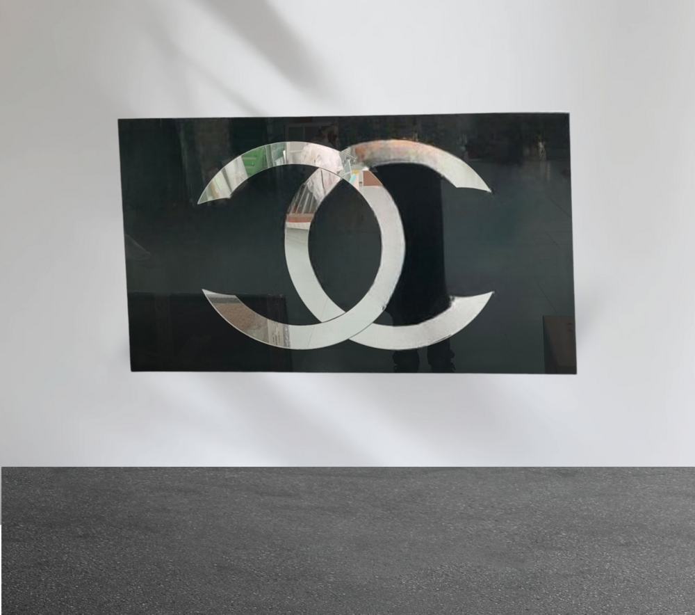 Logotipo de Chanel en plata sobre fondo rectangular negro, montado en una pared blanca.