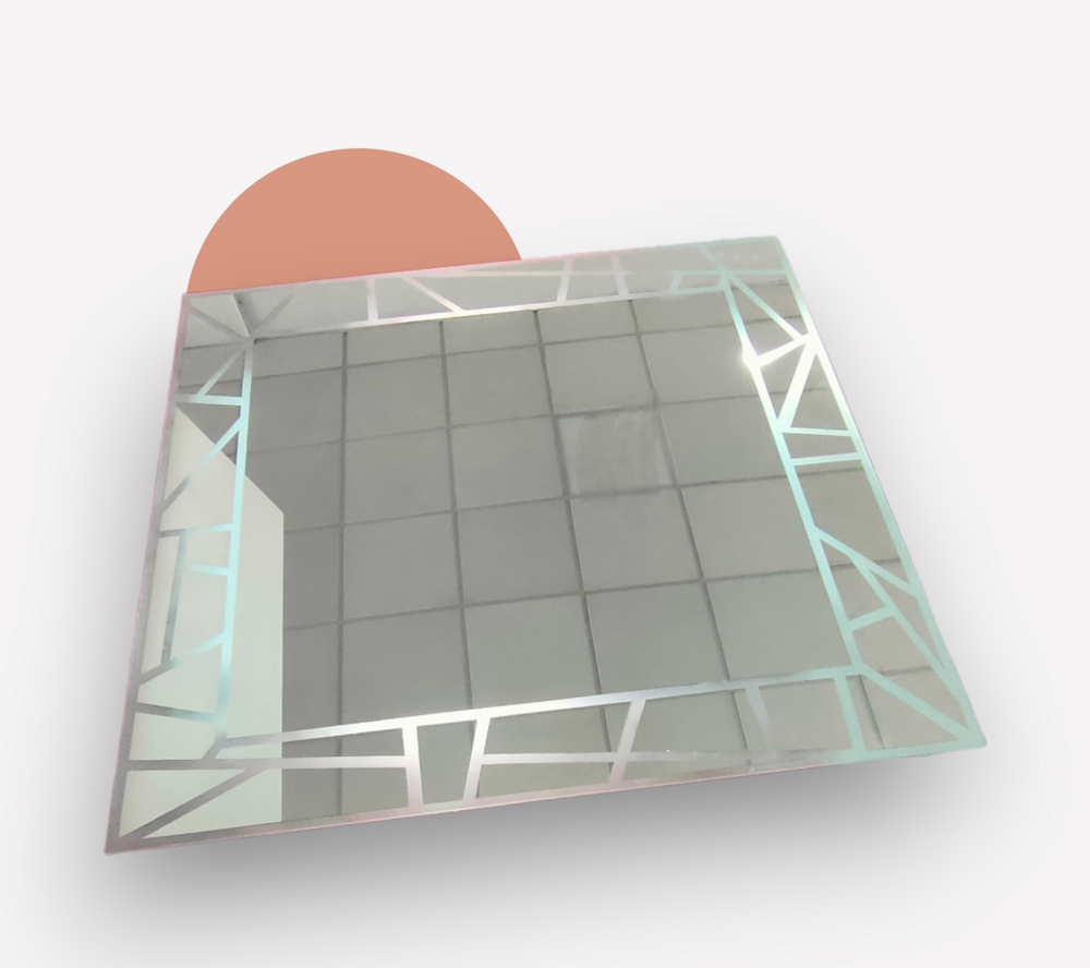 Espejo cuadrado con borde de diseño geométrico, que refleja un suelo de baldosas.