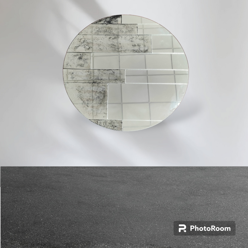 Espejo de mosaico redondo sobre pared blanca, suelo gris oscuro.