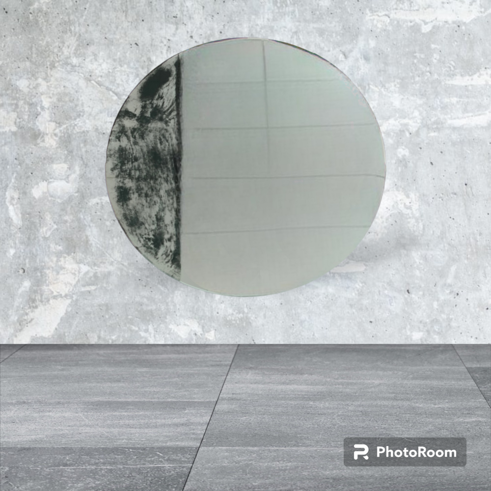 Espejo circular, mitad patrón abstracto negro, colgado en una pared de hormigón gris sobre un suelo de baldosas grises.