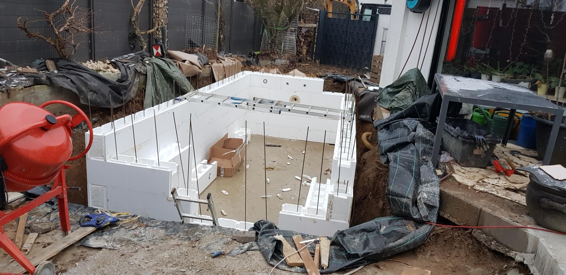 Errichtung einer rechteckigen Struktur in einem Hof mit weißen Schaumstoffblöcken und einem Betonmischer.