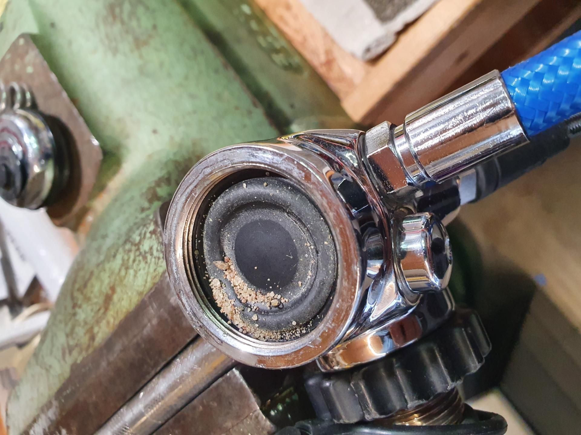 ein Reglers mit einem blauen Schlauch, der an ein Metallarmatur angeschlossen ist; im Inneren sind Ablagerungen zu sehen.