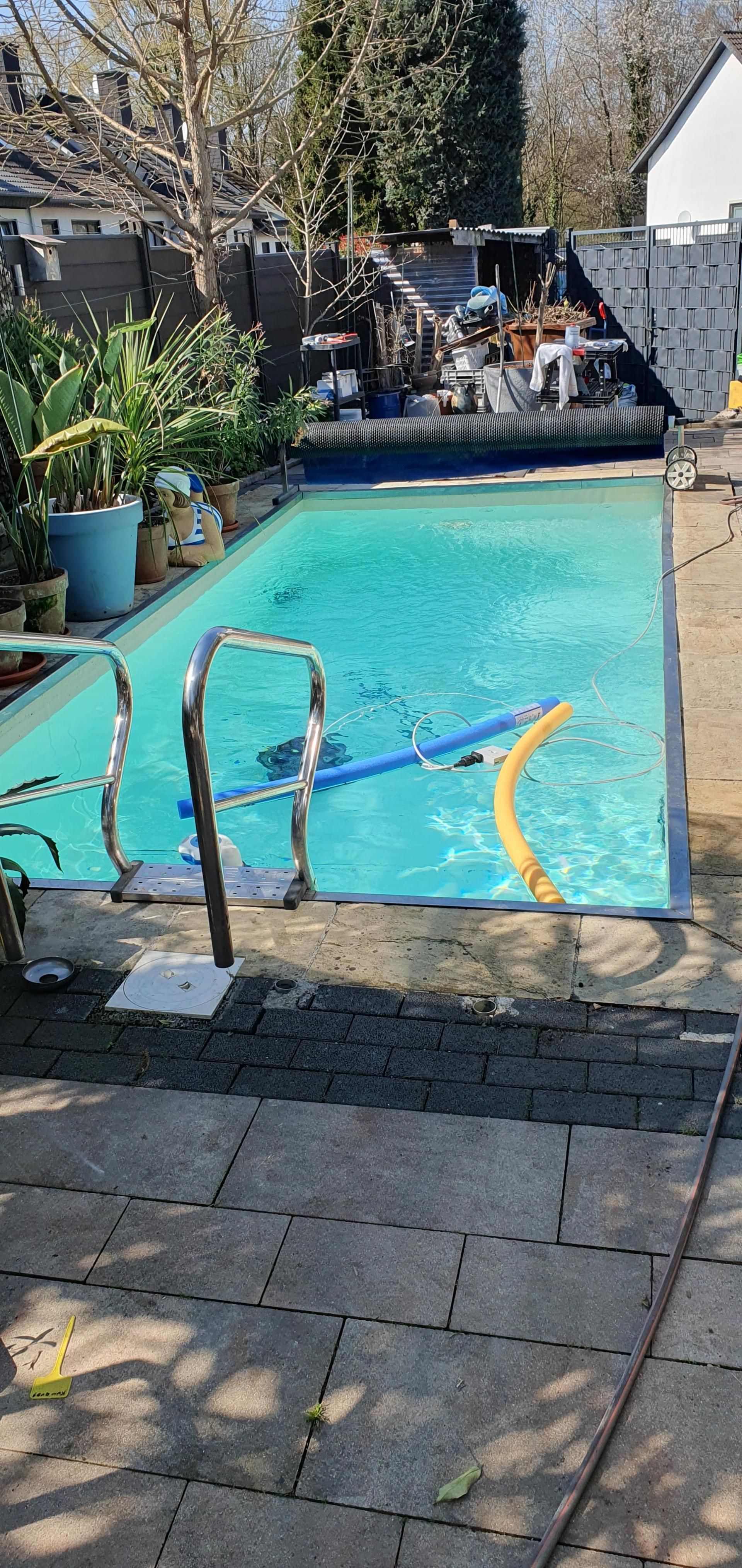 Ein rechteckiger Swimmingpool, gefüllt mit türkisfarbenem Wasser, in einem Garten.