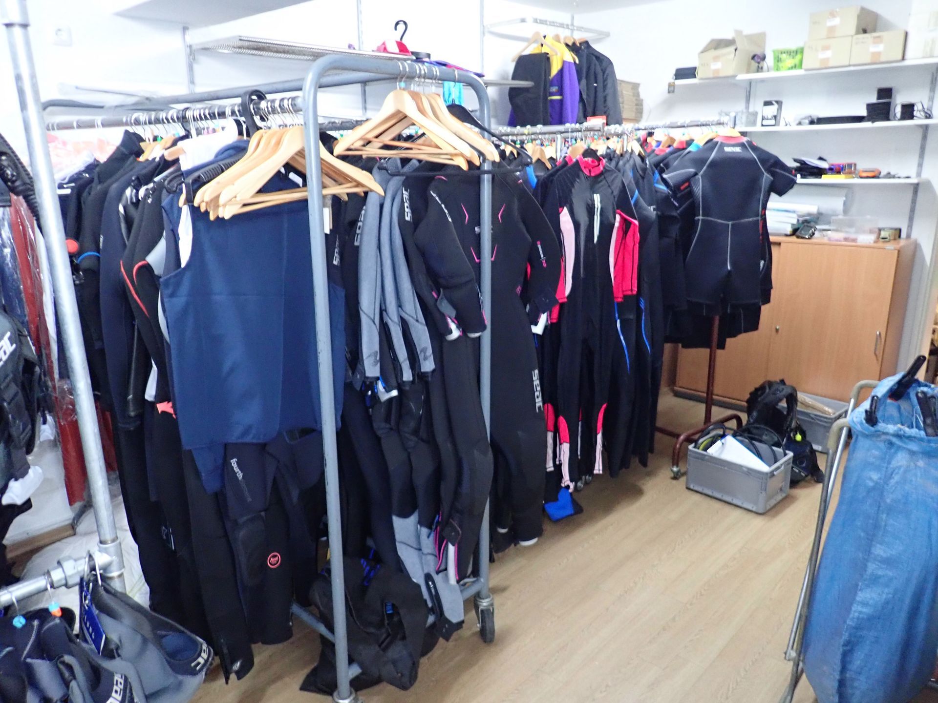 In einem Geschäft hängen an Kleiderständern verschiedene Neoprenanzüge und andere Kleidungsstücke. 