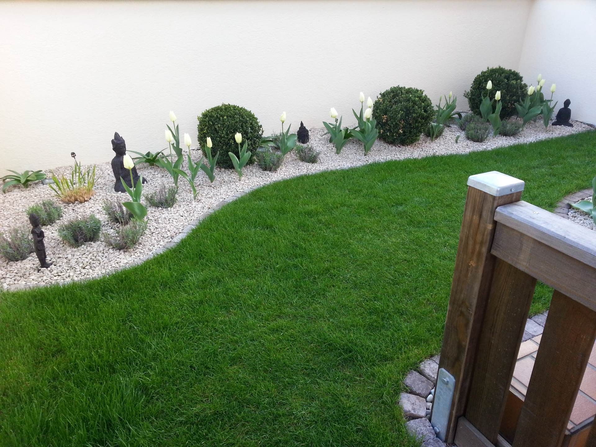 Gepflegter Garten mit grünem Rasen, weißem Kiesbeet, Tulpen, Buchsbaumkugeln und mehreren kleinen schwarzen Hasenfiguren.