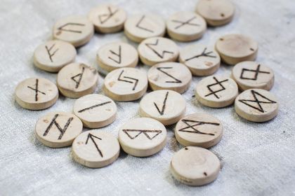 Piedras rúnicas de madera con símbolos grabados dispuestos sobre una tela gris claro.