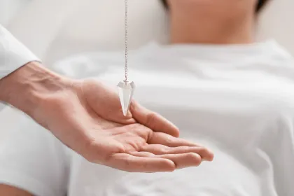 Mano sosteniendo un péndulo de cristal sobre una persona acostada.