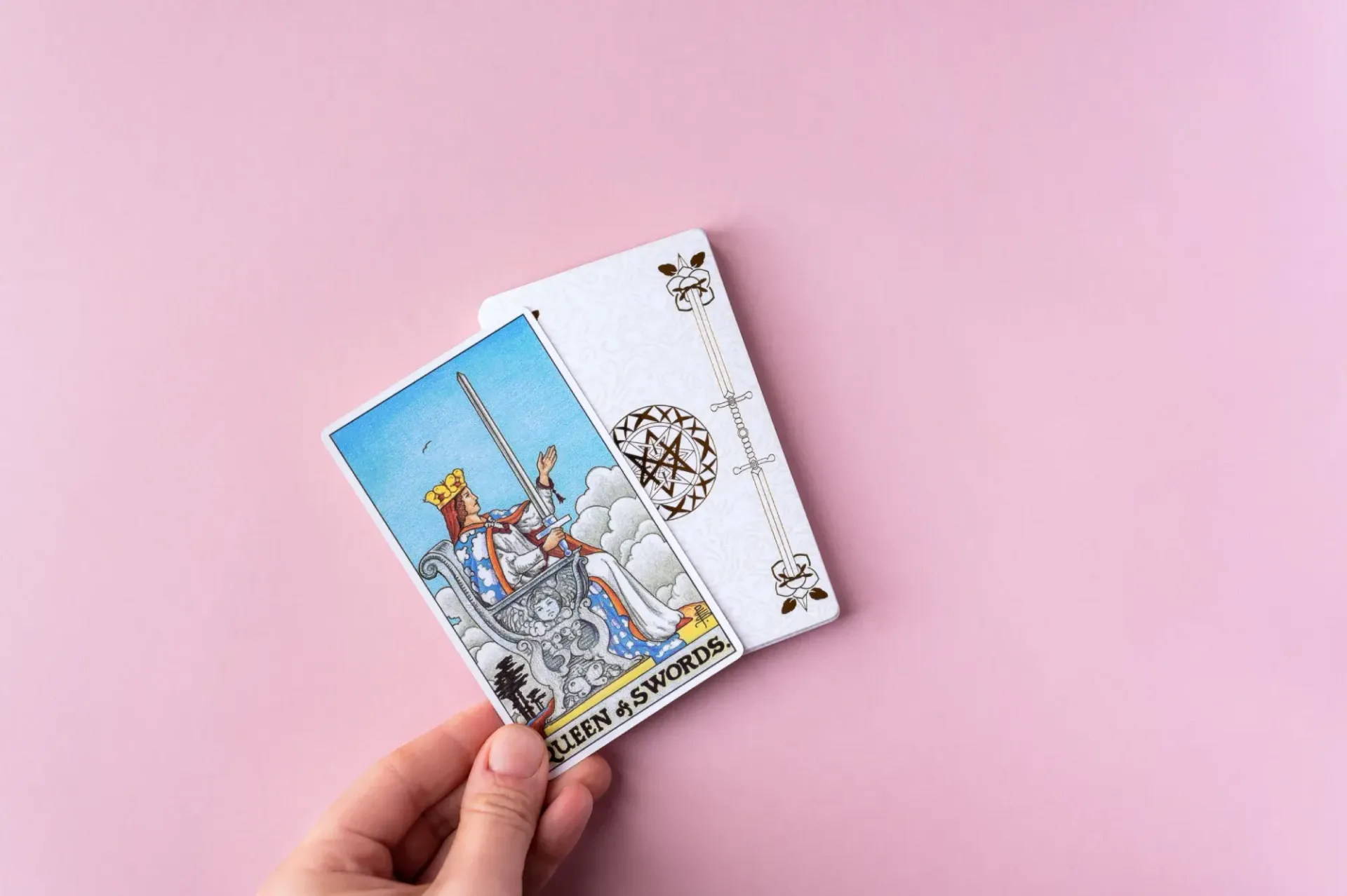 Mano sosteniendo una carta del tarot que muestra a El Emperador; fondo rosa, otras cartas en el fondo.