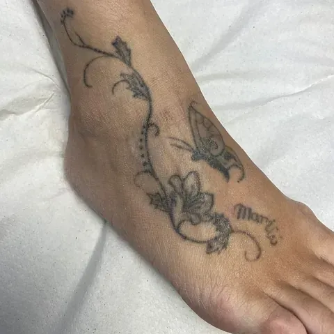El pie de una mujer tiene un tatuaje de flores y una mariposa.